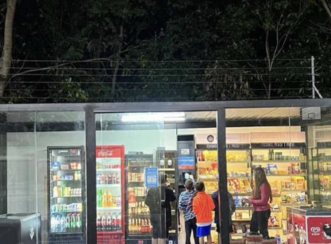 Fachada iluminada de um mini mercado autônomo à noite, com clientes na loja